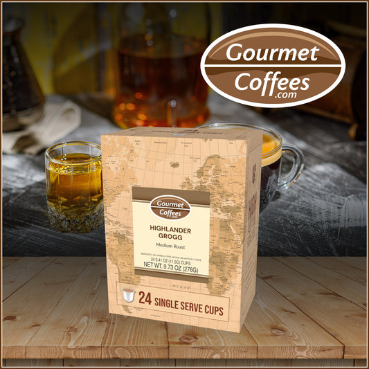 Gourmet Coffees Highlander Grogg package on a wooden surface with a glass of amber liquid and a cup in the background.